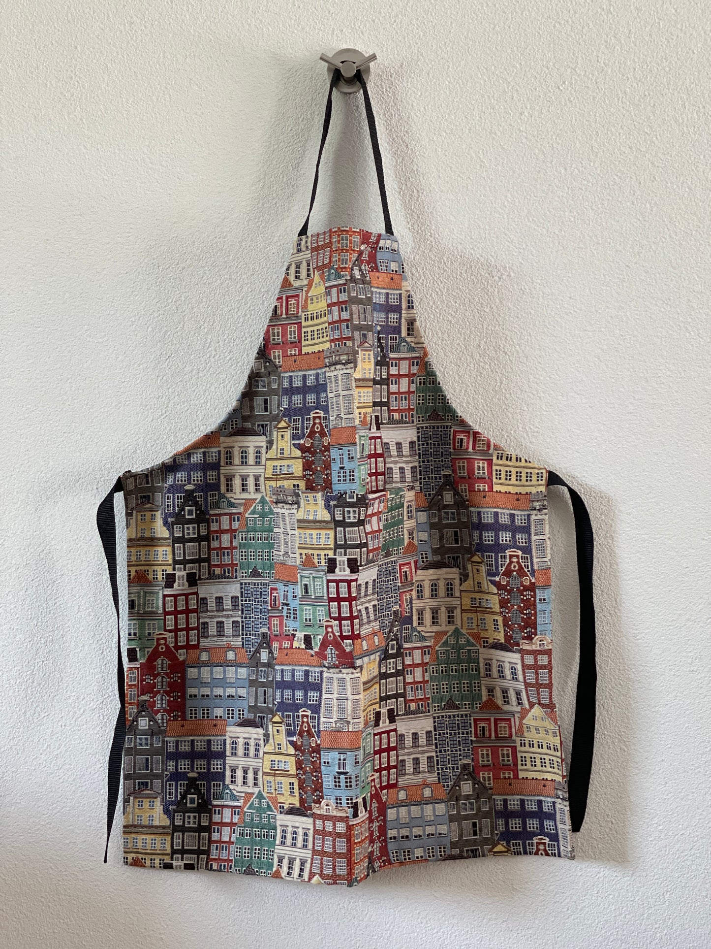 A multicolored apron with a cityscape pattern, hanging on a hook.