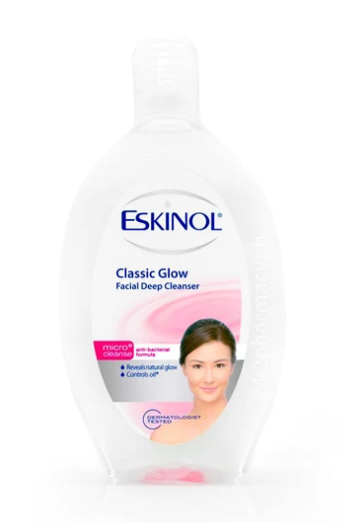 A bottle of ESKINOL Classic Glow Facial Deep Cleanser, featuring a white bottle with a clear cap and a label containing blue and pink text, a pink swoosh, and a photo of a woman's face.