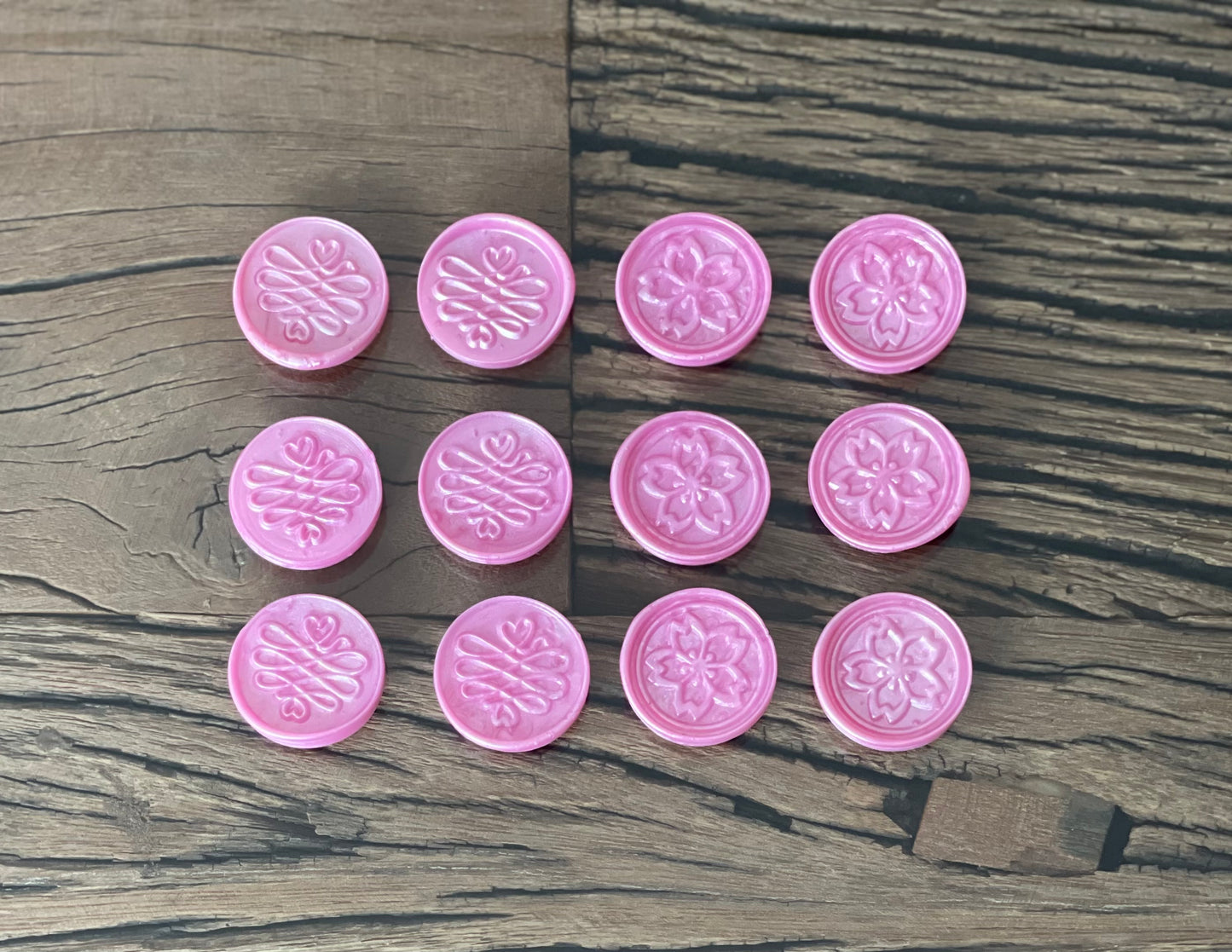 A collection of pink sealing wax stamps with floral patterns, placed on a wooden surface.