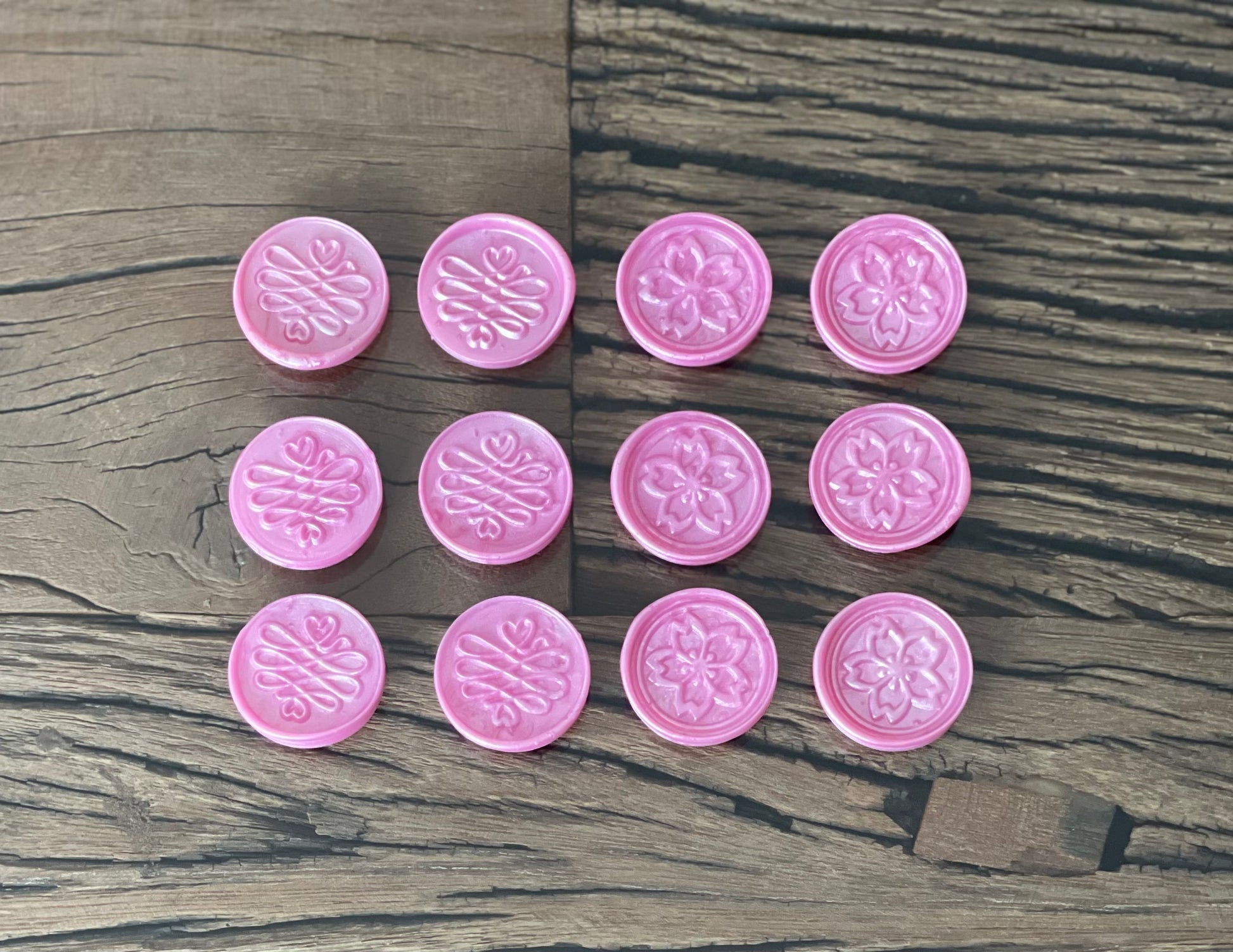 A collection of pink sealing wax stamps with floral patterns, placed on a wooden surface.