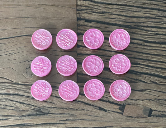 A collection of pink sealing wax stamps with floral patterns, placed on a wooden surface.